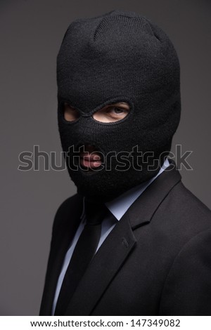 White collar crime. Portrait of businessman in black balaclava looking at camera while isolated on grey