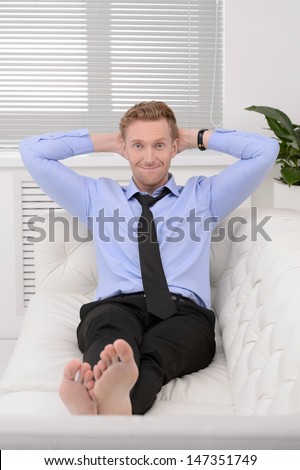 Relaxing after working day. Cheerful young businessman relaxing on the couch and holding his head in hands