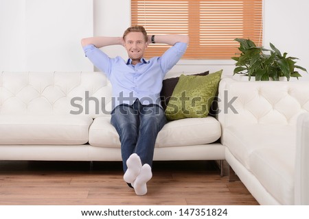 Doing nothing at his day off. Cheerful young men sitting on the couch with his head in hands