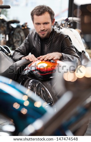 Customer examining motorcycle. Cheerful young men in leather clothing examining motorcycle before buying