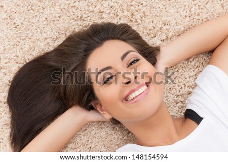 Women lying on the floor. Top view of cheerful young women lying on the carpet with her head in hands and smiling at camera