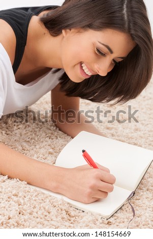 Making notes. Cheerful young women lying down on the floor and making notes at her note pad
