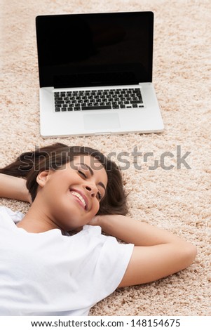 Leisure time. Top view of cheerful young women lying down near her laptop with her head in hands