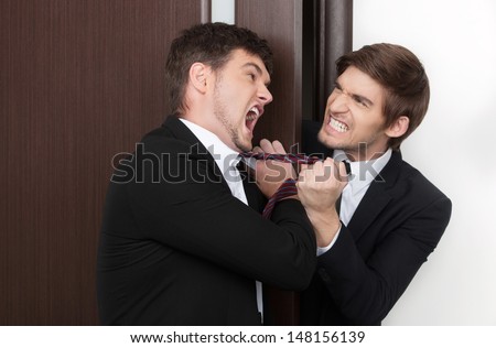 Office conflict. Two angry young business men fighting at office