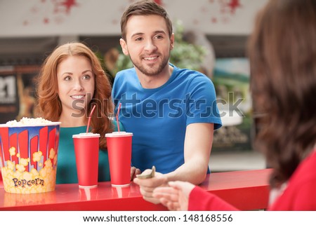 Loving couple at the restaurant. Young loving couple buying popcorn and soda at the cinema bar
