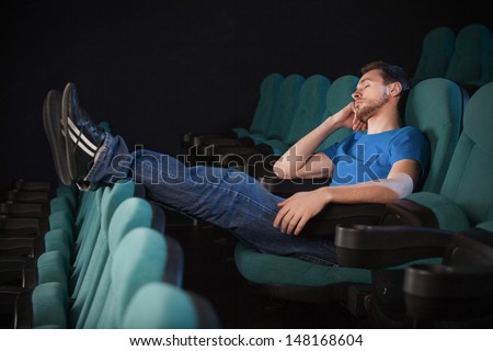 Sleeping at the cinema.  Side view of young men sleeping at the cinema and holding his hand on chin
