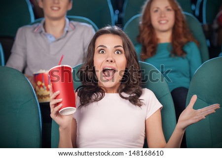 Excited women at the cinema. Beautiful young women drinking soda and gesturing while watching movie at the cinema