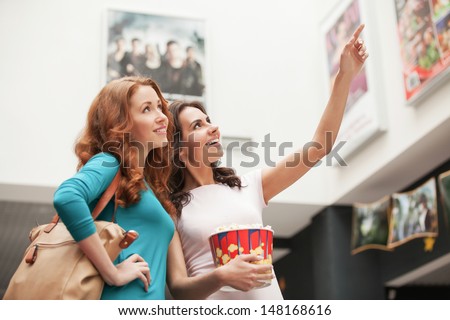 Friends Choosing Movie At The Cinema. Beautiful Young Female Friends Choosing Movie To See At The Cinema