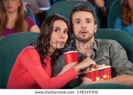 Great movie! Young couple eating popcorn and drinking soda while watching movie at the cinema
