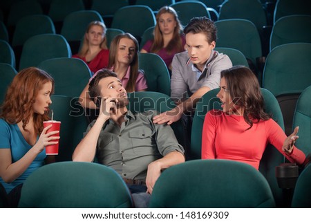 Stop talking! Young men talking at phone while watching movie at the cinema