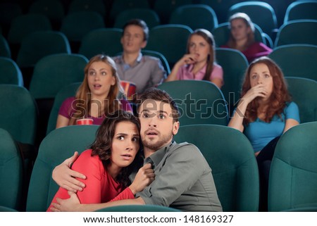 Horror movie. Terrified young couple hugging while watching movie at the cinema