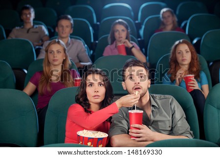 Great movie! Young couple feeding each other while watching movie at the cinema