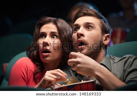 Horror movie. Terrified young couple eating popcorn while watching movie at the cinema