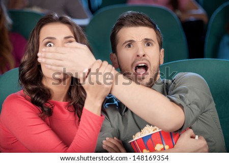 Don\'t look at this! Shocked young couple watching movie at the cinema while men covering his girlfriend\'s eyes with hands