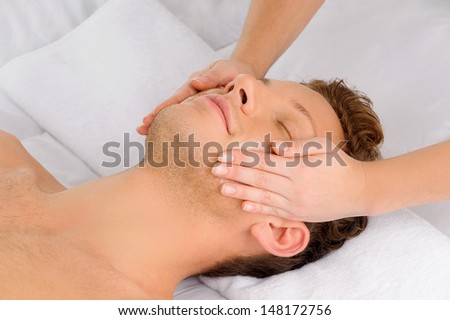 Facial massage. Top view of relaxed young men lying on the massage table while massage therapist massaging his face