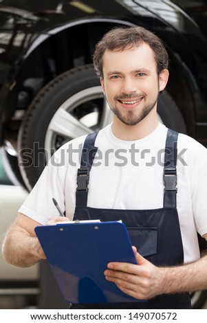 Mechanic with clipboard. Cheerful young auto mechanic holding a clipboard in his hands and smiling