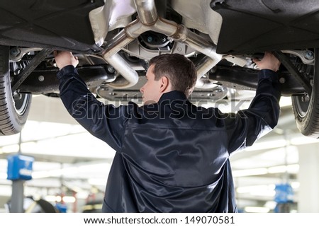 Mechanic at work. Confident auto mechanic working at the repair shop while standing under the car