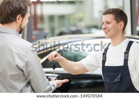 Auto mechanic and customer. Cheerful auto mechanic giving a car key to customer and smiling