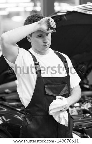 Tired auto mechanic. Tired auto mechanic holding a handkerchief and holding his hand on the forehead