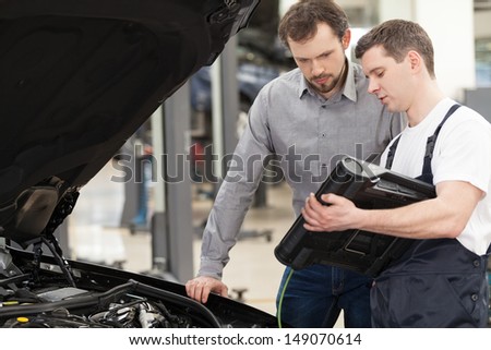 Examining a car. Confident auto mechanic explaining something to a customer while standing near the car