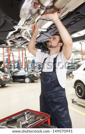 Confident mechanic at work. Confident young mechanic working at the repair shop while standing under the car