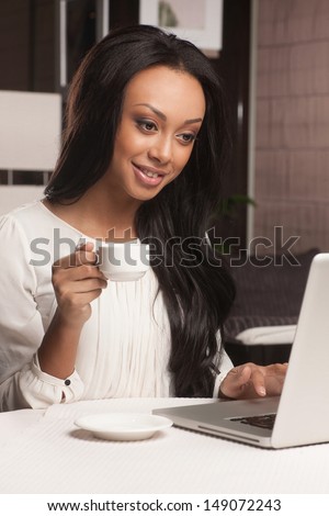 Women working on laptop. Beautiful African descent women drinking coffee and working on laptop