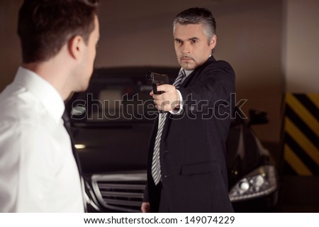 Dirty business. Confident mature men in formalwear aiming another men with gun