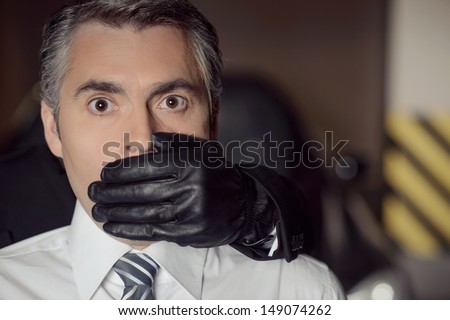 Kidnapping. Aggressive young men covering businessman mouth with his hand in glove