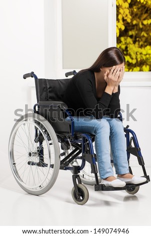 Women with disability. Depressed young women sitting at the wheelchair and covering her face with hands