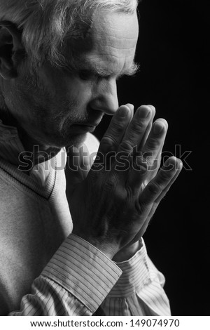 Senior man praying. Black And White image of senior men praying and holding his hands clasped while isolated on black