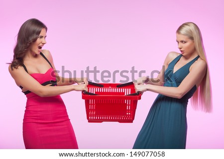 ItÃ?Â¯Ã?Â¿Ã?Â½ mine! Two angry young women trying to take away one shopping basket while isolated on pink background