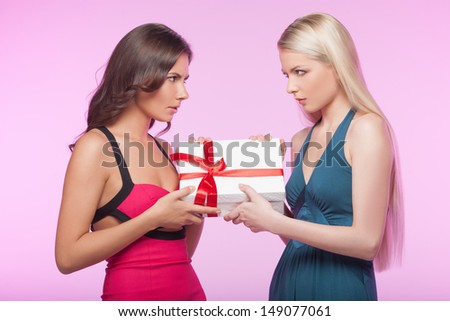This box is mine! ItÃ?Â¯Ã?Â¿Ã?Â½ mine! Two angry young women trying to take away one gift box while isolated on pink background