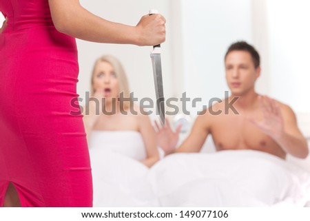 Ready for revenge! Rear view of young women holding a knife while her boyfriend lying on the sofa with another women