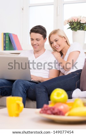 Using computer together. Beautiful young couple sitting close to each other and looking at the laptop