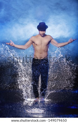 Dancing in water. Young male dancer in black fedora dancing on the wet floor