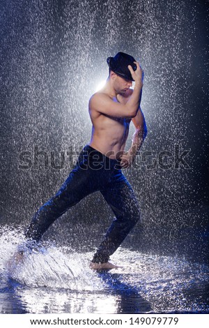 Dancing in the rain. Young male dancer in black fedora dancing under the rain