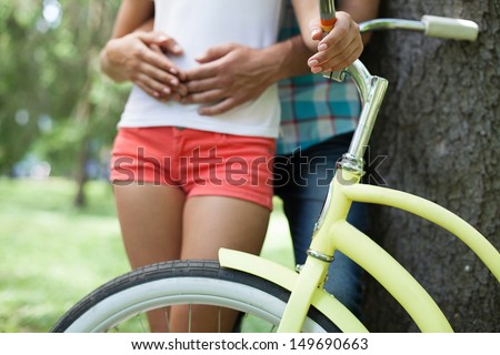 Couple in park. Cropped image of loving couple hugging near tree while woman holding her hand on bicycle