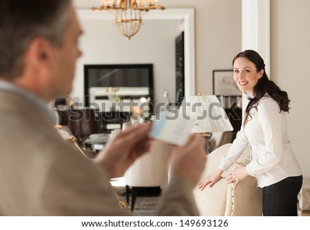 Thinking About A Price. Thoughtful Middle-Aged Man Holding A Price While Standing Near His Wife At The Furniture Store