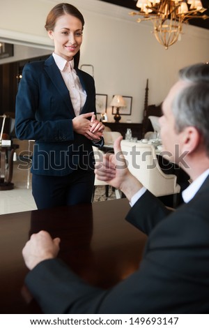 Man and sales clerk. Confident mature man in formalwear gesturing while communicating with sales clerk