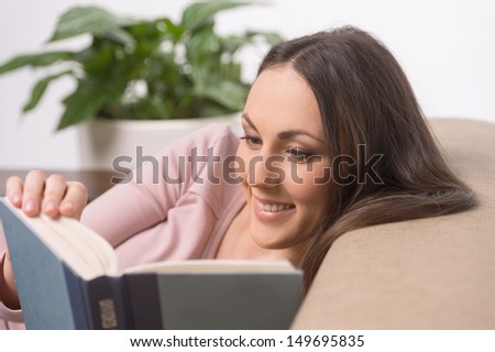 Exciting book. Cheerful young woman reading a book while lying on a couch