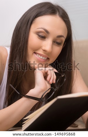 Such an interesting book! Portrait of cheerful young woman reading a book and holding glasses