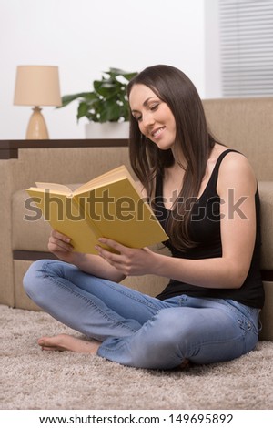Reading at home. Beautiful young woman sitting on the floor at home and reading book