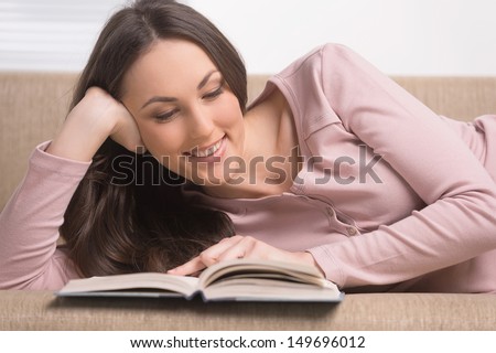 Woman reading a book. Cheerful young woman reading a book while lying on the couch