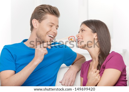 Eating sushi together. Beautiful couple eating sushi while sitting close to each other on the couch