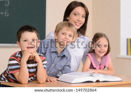 Teacher and pupils. Confident young teacher sitting together with pupils and reading book