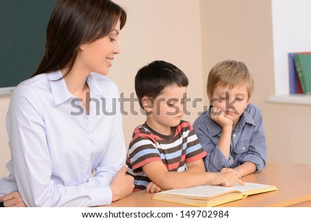 Reading together. Cheerful young female teacher sitting near two schoolboys reading a book