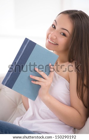 It is her favourite book. Beautiful young cheerful woman holding a book and smiling