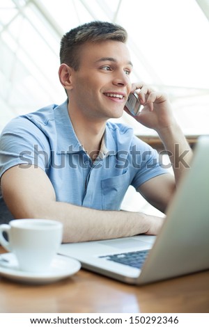 Young man in restaurant. Cheerful young man talking on the mobile phone and smiling while sitting at the restaurant