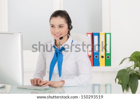 Customer service representative. Cheerful young female customer service representative in headset working at the computer and smiling