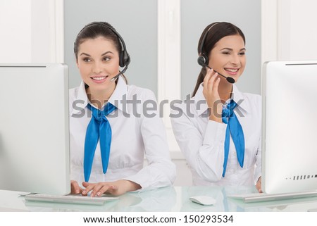Two customer service representatives at work. Two cheerful young female customer service representatives in headset working at the computer and smiling
